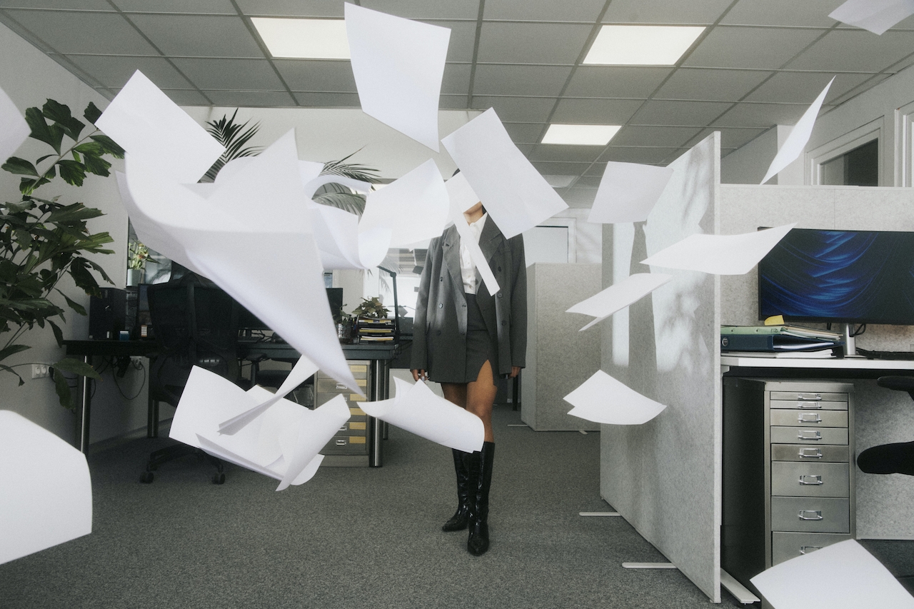 A woman stands in the middle of a flurry of white paper in an office. Used for a promotional image on Cool Copy Club's 2024 Digital Marketing trend predictions.