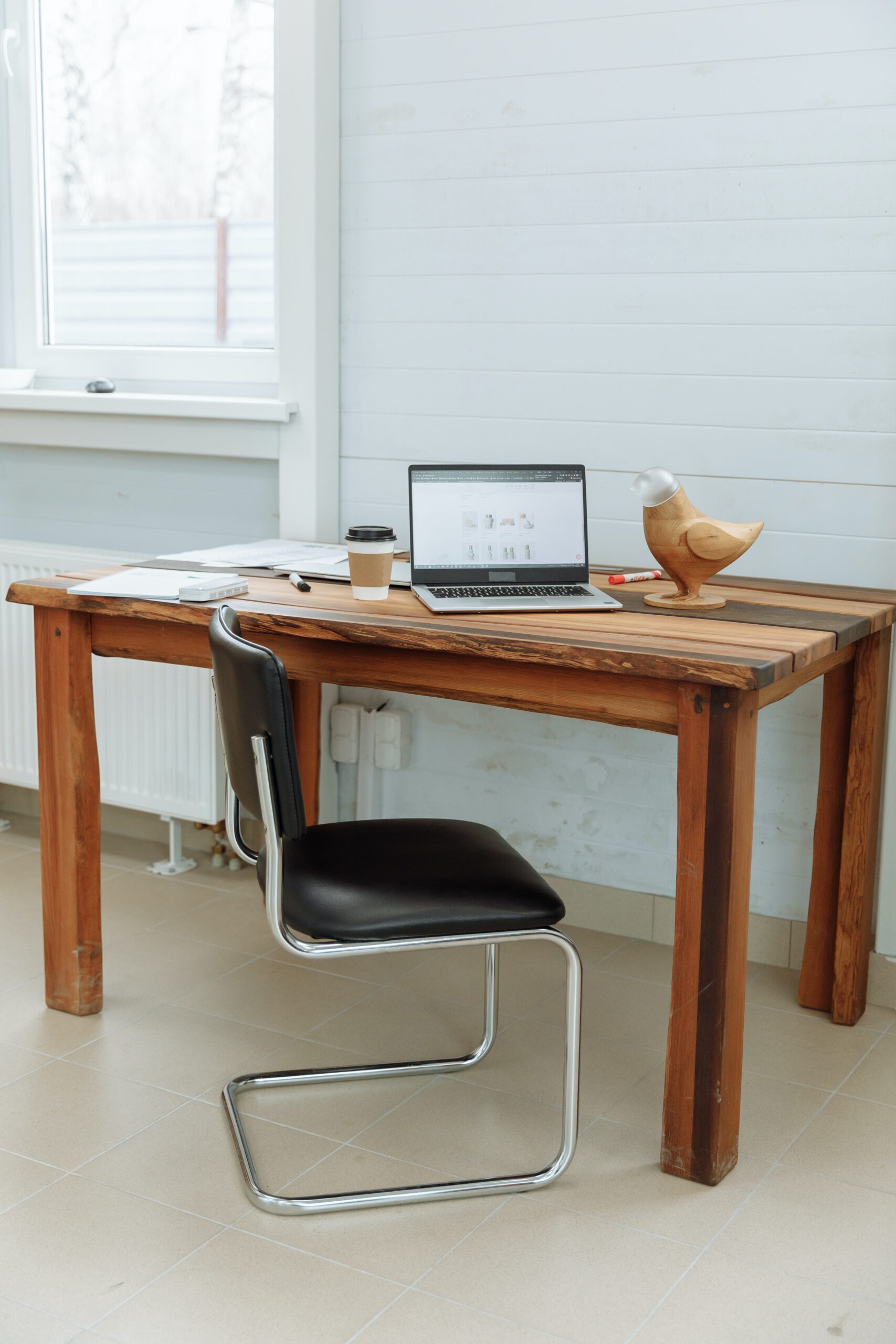 A desk with a laptop on it and a black chair in front of it, used as the promotional image for a blog post on whether it's better to DIY or hire out your business' website copy.